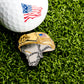 A close-up of a golf ball with an American flag design and the Ballmarkers.com Combat Helmet Ball Marker, both displayed on green artificial grass, showcases this unique military-themed golf accessory.
