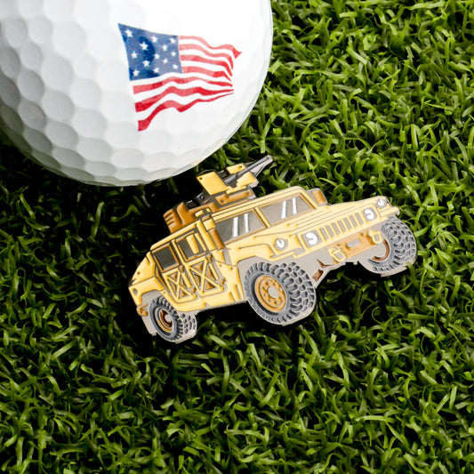 A close-up of the Humvee Ball Marker by Ballmarkers.com, featuring an American flag on a golf ball beside a yellow toy military vehicle on green grass, brings bold tactical style to your game.
