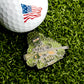Show your love for the USA with the Sniper Ball Marker from Ballmarkers.com, featuring an American flag golf ball on artificial grass and a sniper in a ghillie suit holding a rifle by the pin.