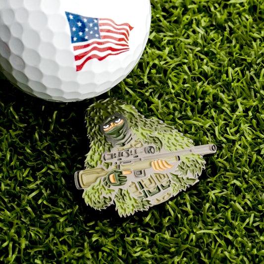 Show your love for the USA with the Sniper Ball Marker from Ballmarkers.com, featuring an American flag golf ball on artificial grass and a sniper in a ghillie suit holding a rifle by the pin.