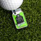 A close-up of a golf ball next to the Logie Joe's Golf Moonshine Ball Marker on bright green artificial grass, highlighting fun and unique golf accessories.