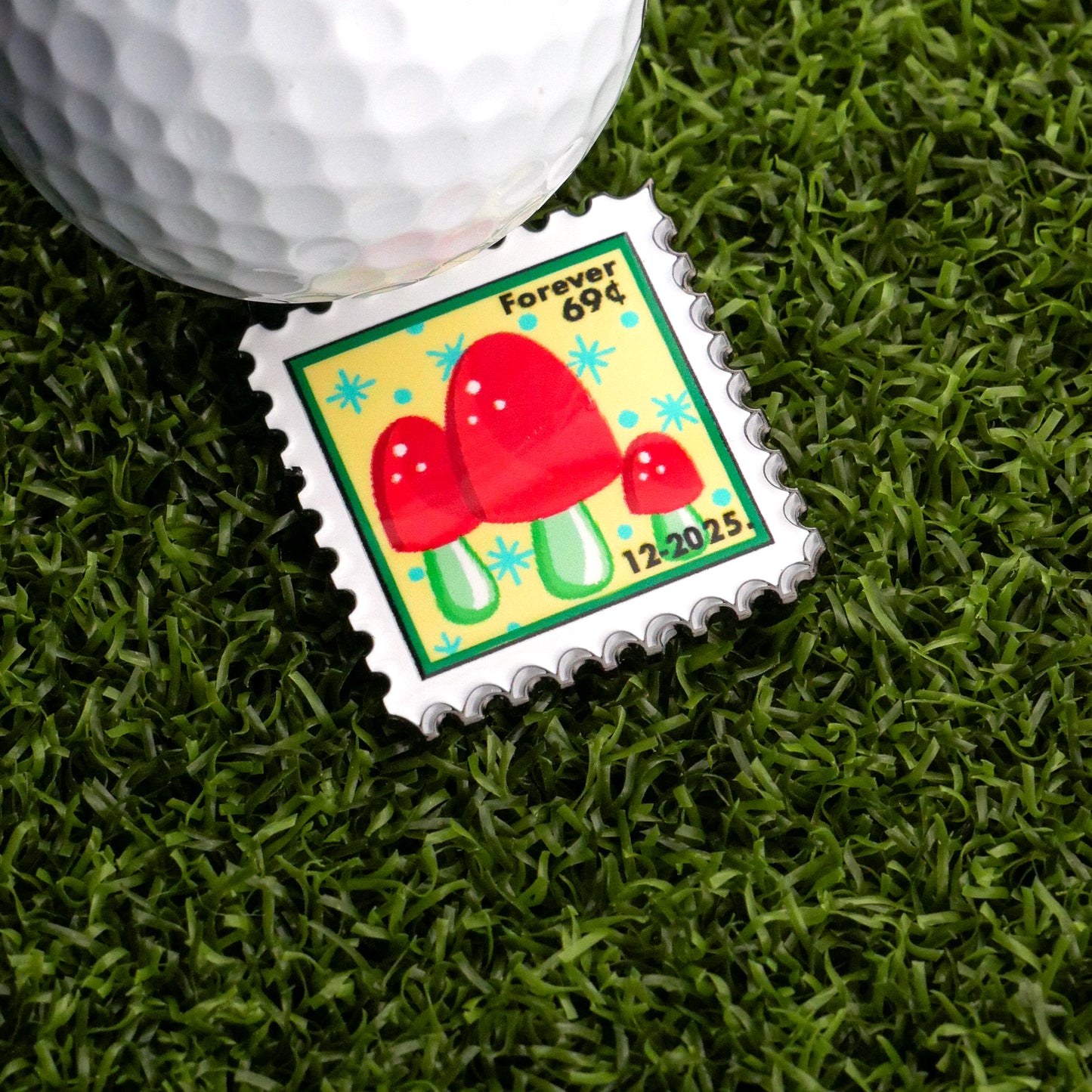 The December Mushroom Stamp Ball Marker by Ballmarkers.com features red mushrooms on a yellow and green background, with "Forever 69¢" and "12.2015" text—ideal as a unique golf ball marker for your game.