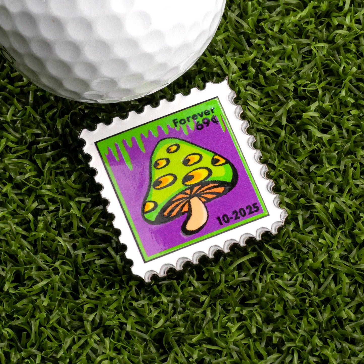The 10-2025 Mushroom Stamp Ball Marker by Ballmarkers.com features a yellow and green mushroom with a brown stem on purple, reading "Forever 99¢"—a unique golf accessory beside your ball on the green.