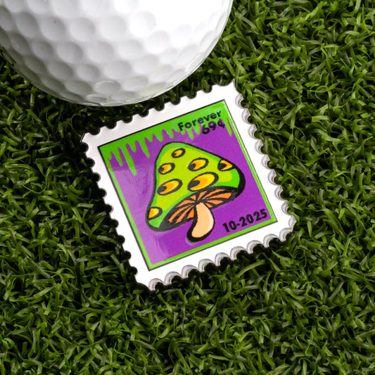 The 10-2025 Mushroom Stamp Ball Marker by Ballmarkers.com features a yellow and green mushroom with a brown stem on purple, reading "Forever 99¢"—a unique golf accessory beside your ball on the green.
