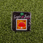 The Mushroom Stamp 08/2025 by Logie Joe’s Golf is a square enamel ball marker, styled like a postage stamp with a red mushroom and yellow background, marked “Forever 69¢, 8-2025,” packaged on brand card atop green artificial grass.