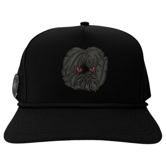 Introducing Logie Joe's Golf Night Stalker Golf Hat: a black snapback cap with a shaggy creature and bright pink animal eyes patch, black rope detail, adjustable fit, and built-in magnetic ball marker holder plus marker included.