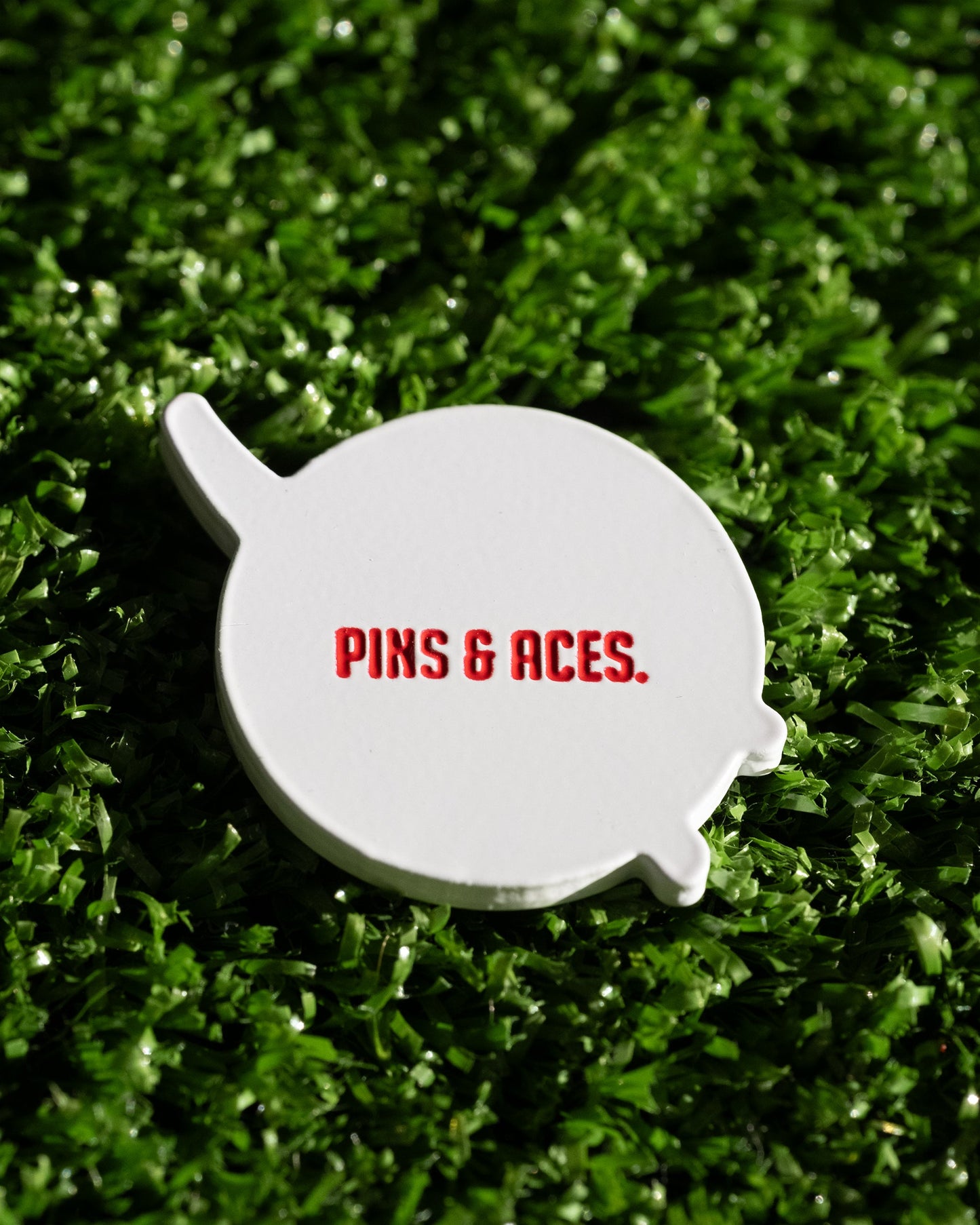 The NASA "Meatball" Ball Marker by Pins and Aces features the iconic red logo on a white marker, resting on green turf for a standout addition to your golf accessories.
