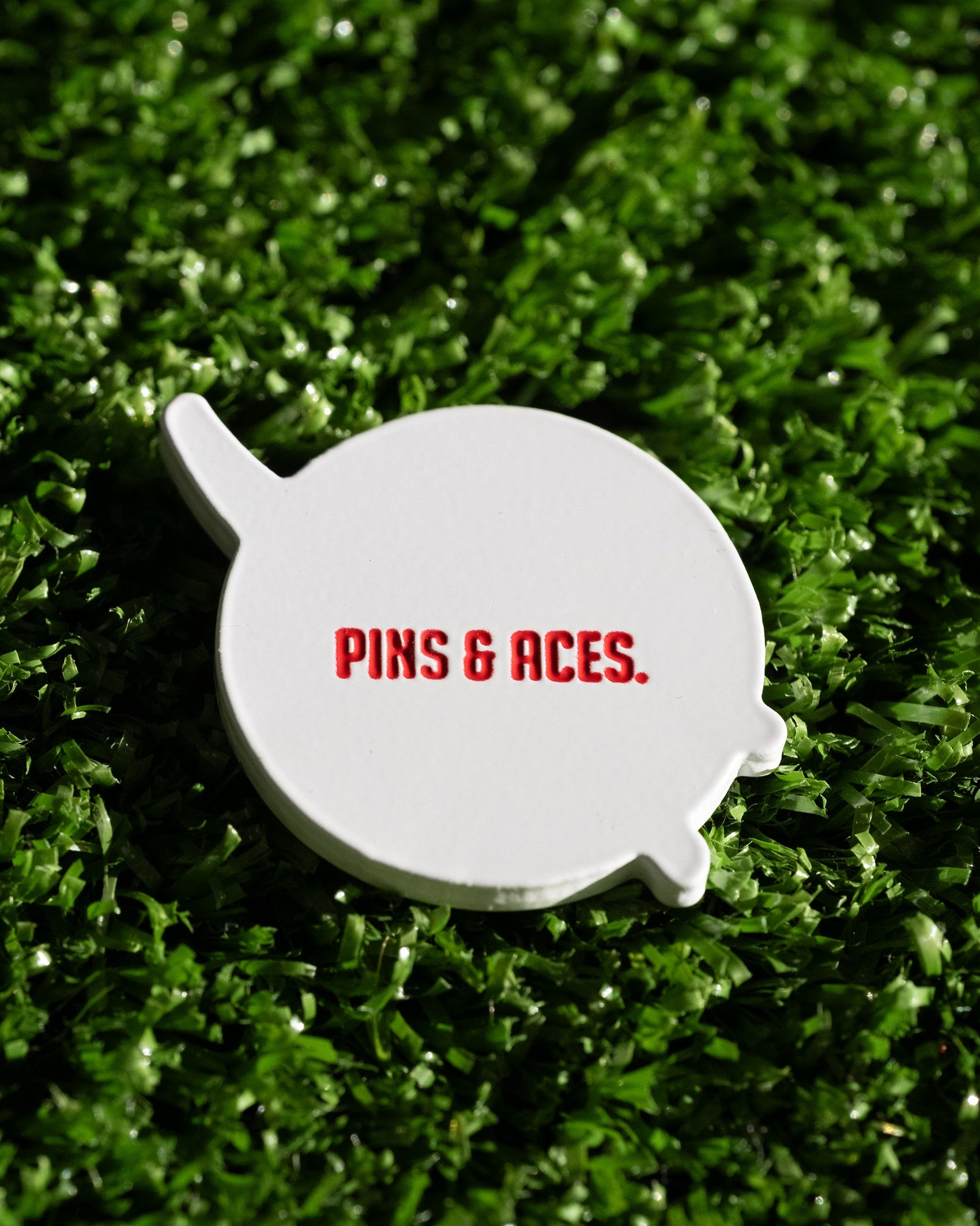 The NASA "Meatball" Ball Marker by Pins and Aces features the iconic red logo on a white marker, resting on green turf for a standout addition to your golf accessories.