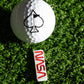 A white golf ball with a black spade sits on green turf above the Pins and Aces NASA "Worm" Ball Marker, styled as an enamel NASA pin.