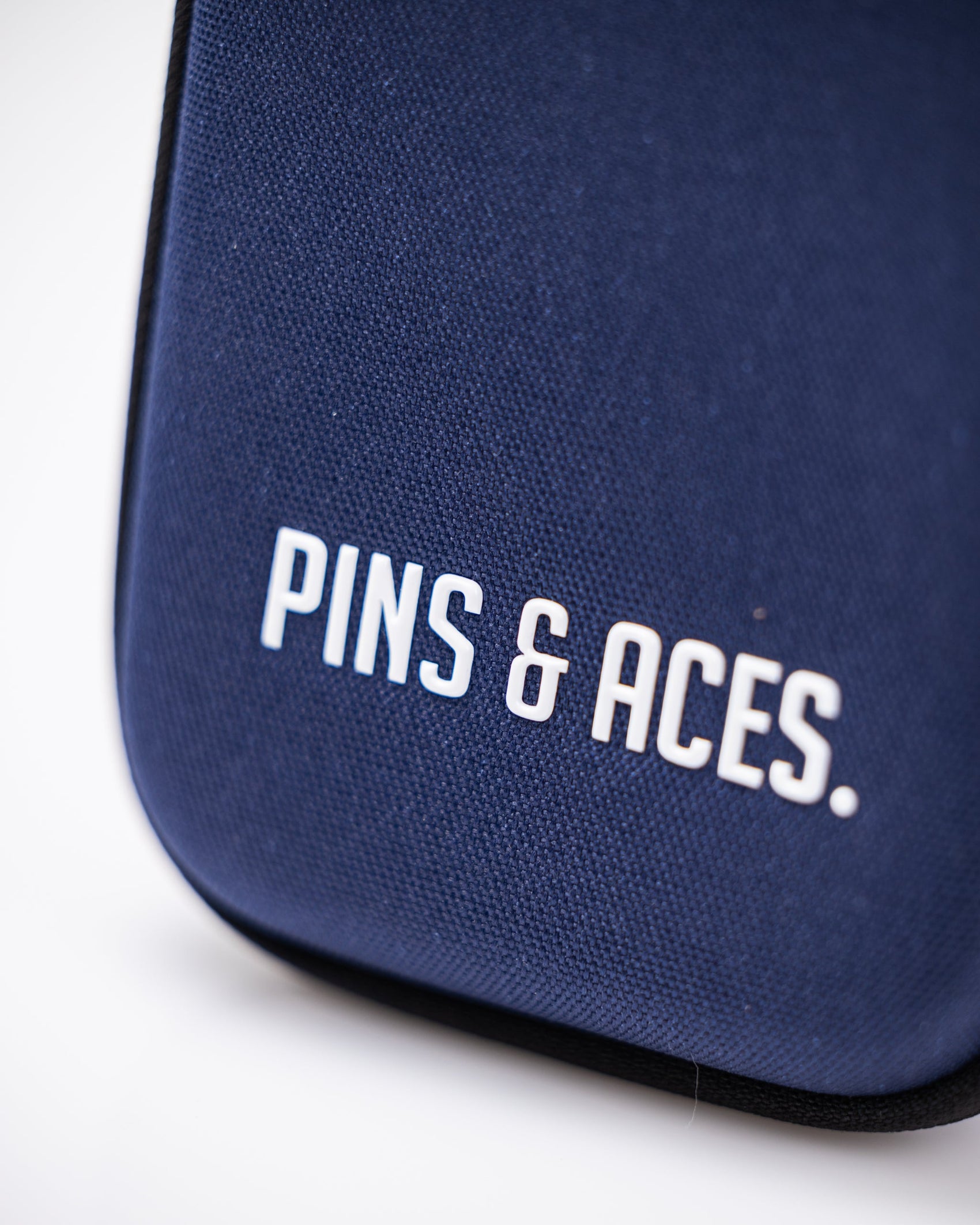 Close-up of the Pins and Aces Glove & Accessory Caddie in navy, featuring white "PINS & ACES." text, rounded edges, and a smooth texture.