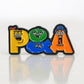 The Pins and Aces P&A Buddies Ball Marker features colorful enamel letters, each with a unique cartoon face in yellow, green, and orange. Its reflective white background is perfect for displaying on any magnetic surface.