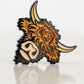 The Highland Cow Ball Marker by Pins and Aces is a cast metal enamel pin shaped like a Highland cow's head, featuring orange, brown, and cream enamel with black outlines, displayed on a reflective white surface.