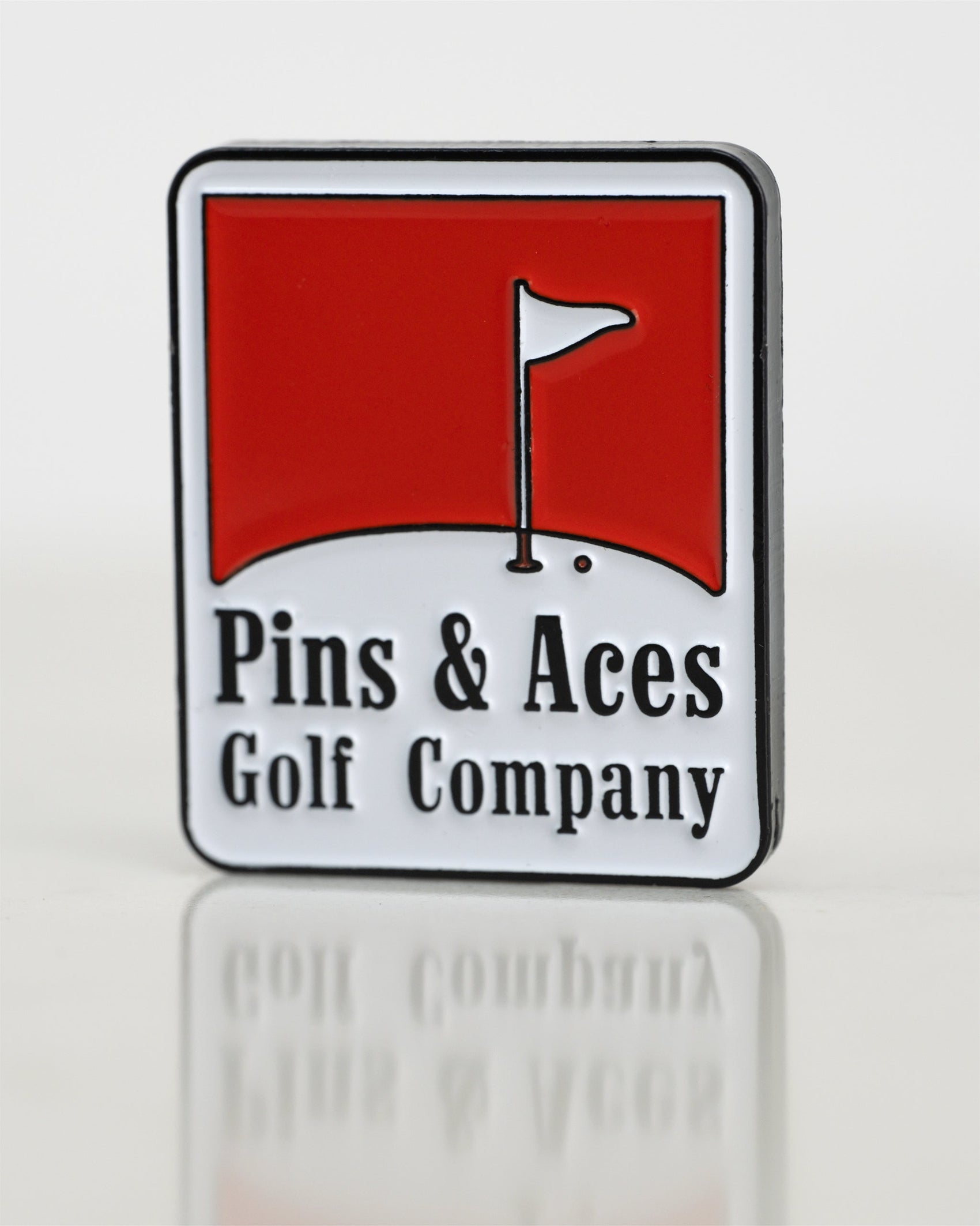 The Pins and Aces Pins Reds Ball Marker is a rectangular enamel badge featuring a red and white design with a golf flag on green, plus "Pins & Aces Golf Company" text below the image.