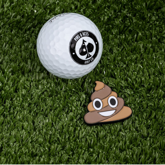 Add a playful touch to your game with the Poop Ball Marker by Pins and Aces—a white golf ball, enamel finish ball marker, and cartoon poop emoji logo rest on green artificial grass for a fun golfing accessory.