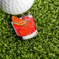A golf ball on artificial grass sits beside the Ballmarkers.com Old Fashioned Ball Marker, a colorful enamel pin shaped like a cocktail with ice cubes, an orange slice, and a cherry garnish.