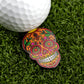 An orange golf ball from Logie Joe's Golf rests on artificial grass next to the Orange Sugar Skull ball marker, highlighting bold patterns and stylish premium golf accessories.