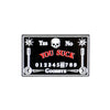 The Ouija Board Ball Marker by Logie Joe's Golf features a black rectangular design with skull, red YES, NO, YOU SUCK phrases, numbers 0–9, and GOODBYE—making it one of the funniest premium golf accessories.