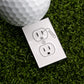 The Shocking Outlet Ball Marker by Ballmarkers.com is a white outlet cover with a golf club and ball design on green artificial grass, paired with a real golf ball that can double as a unique marker.