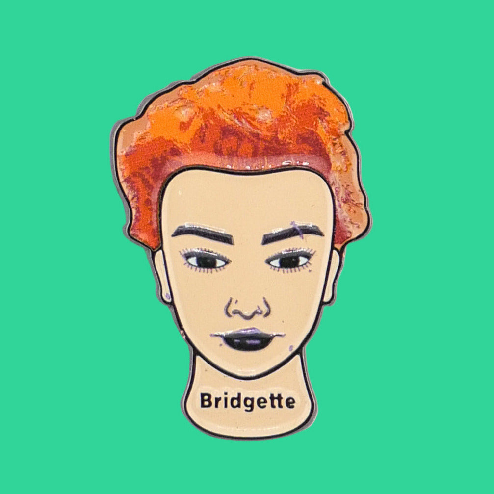 Ball markers by Logie Joes features a stylized face with orange hair, dark eyebrows, and black lipstick. Bridgette is written below on a plain white background.