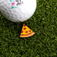 A golf ball with the Logie Joe's Golf logo sits on artificial grass next to the Pepperoni Pizza "Slice" Premium Ball Marker, shaped like a pizza slice.