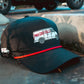 A Logie Joe’s Golf “Free Golf Balls Van” Snapback Hat with a matching ball marker sits on a concrete curb in a parking lot, with shadows and parked vehicles in the background.