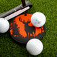 A Logie Joe's Golf Buck Hunter Putting Disk, a golf putter, and three golf balls are arranged on green artificial turf for focused putting practice.