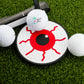 Logie Joe’s Golf Eye Ball Putting Disk, surrounded by a putter and three golf balls on green turf, features a bold red and black eye design—ideal for focused golf practice sessions.