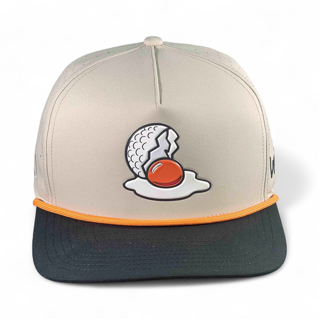 The Logie Joe's Golf Breakfast Ball Snapback Hat + Matching Ball Marker is a beige and black cap with orange trim, featuring an embroidered cracked golf ball that looks like a fried egg and includes a built-in magnet for the marker.