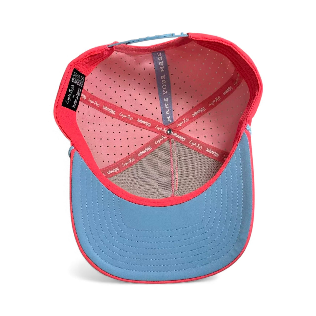 A close-up of the Frosted Elephant Snapback Hat + Matching Ball Marker by Logie Joe's Golf shows its perforated pink lining, interior labels, and stitched brim.