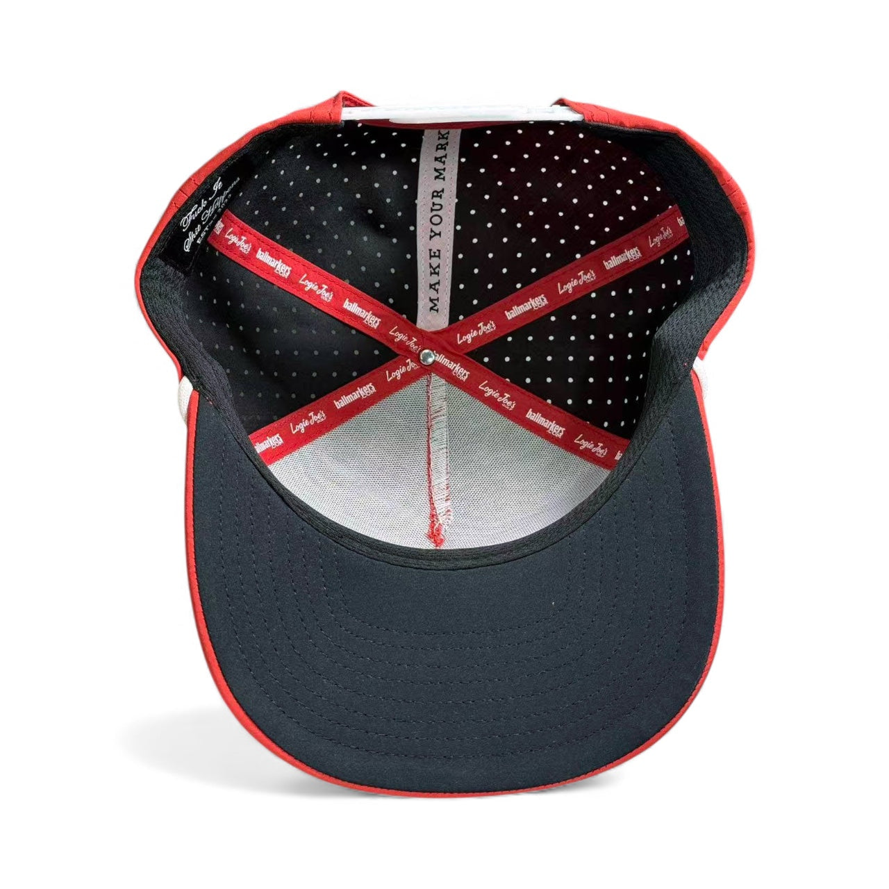 The inside view of the Missing Milk Golf Hat by Logie Joe's Golf shows black fabric with white polka dots, red and white Logie Joe’s bands, and “MAKE YOUR MARK” along the lining—an adjustable red snapback cap with built-in magnetic ball marker.
