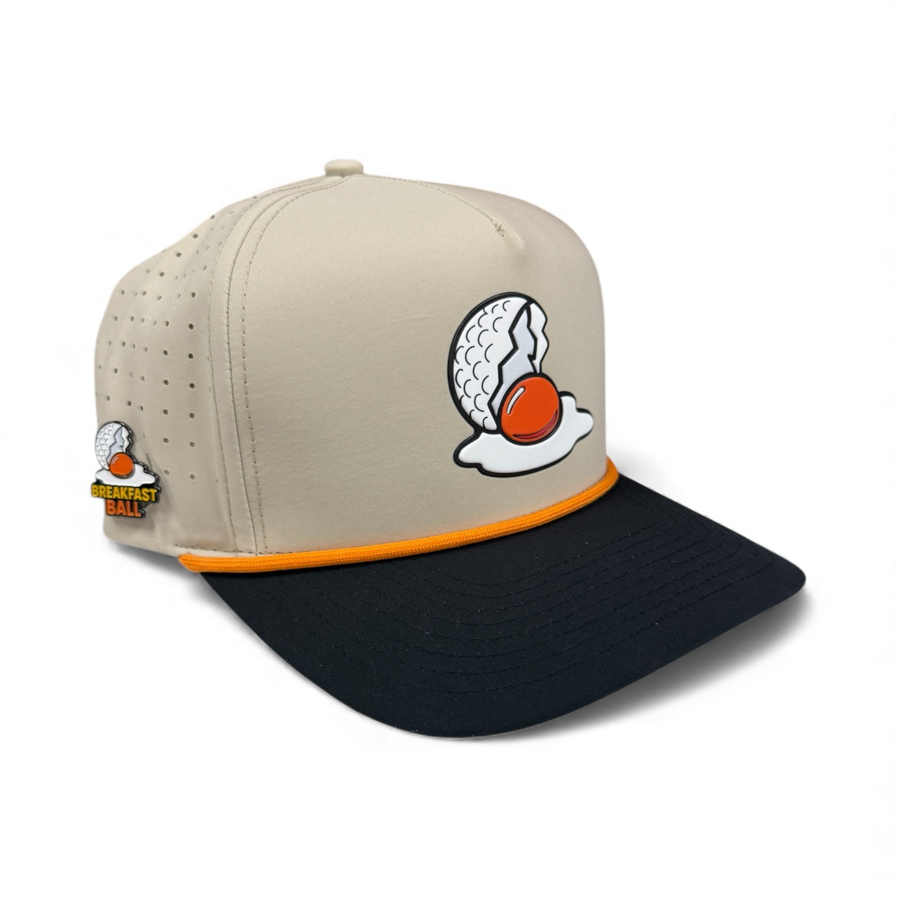 The Logie Joe's Golf Breakfast Ball Snapback Hat + Matching Ball Marker features a beige and black design with a cracked golf ball egg logo, orange accent above the brim, side pin, and built-in magnet for your marker.