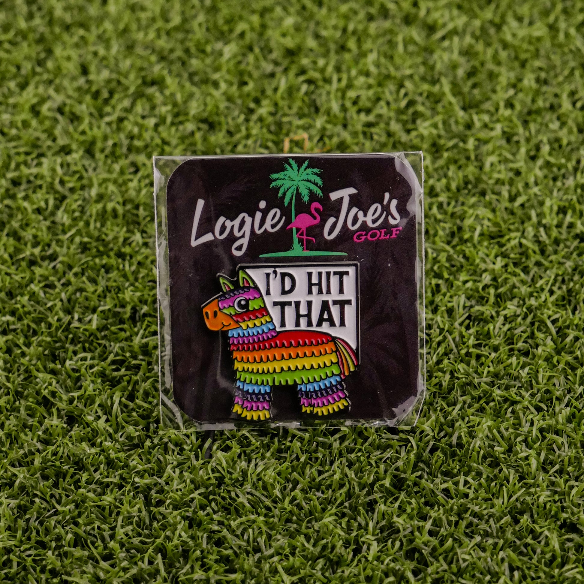 The I’d Hit That Piñata pin by Logie Joe’s Golf features a colorful piñata design with “ID HIT THAT,” displayed on artificial grass. Its backing card shows the Logie Joe’s Golf name with a palm tree and flamingo graphic. Perfect for golf accessory fans.