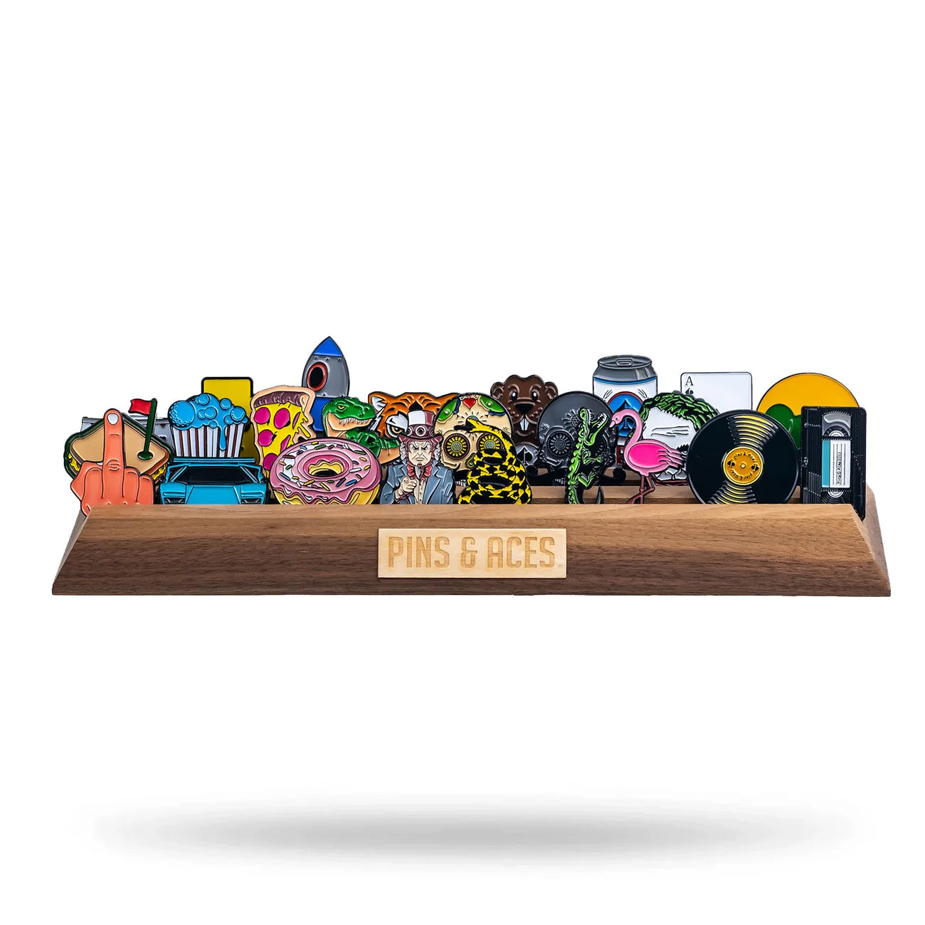 A walnut Ball Marker Display by Pins and Aces presents a colorful lineup of enamel pins—pizza slice, rocket, retro car, donut, vinyl record, cassette tape—neatly arranged in a single row.