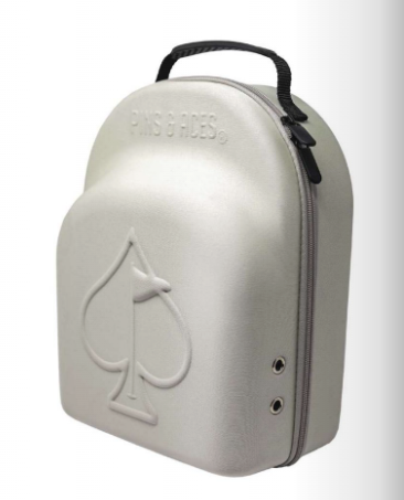 The Hat Caddie by Pins and Aces is a light gray hard-shell golf hat case featuring a raised spade symbol on the front, two side grommets, and a black top handle.