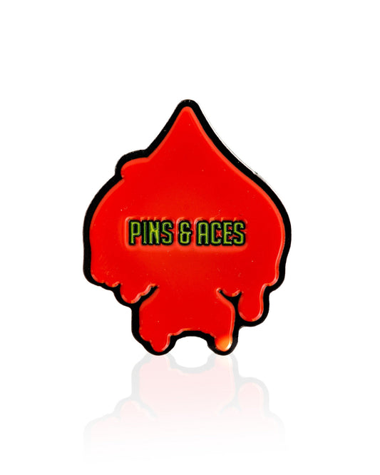 The Flamin' Spade Ball Marker by Pins and Aces is a red, spade-shaped pin with a melted look and bold yellow-green branding. This unique accessory also serves as an ace card ball marker for golfers.