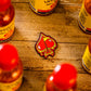 A Pins and Aces Flamin' Spade Ball Marker sits on a wooden surface near several Louisiana hot sauce bottles with red caps, alongside a patch featuring a dripping red spade design.