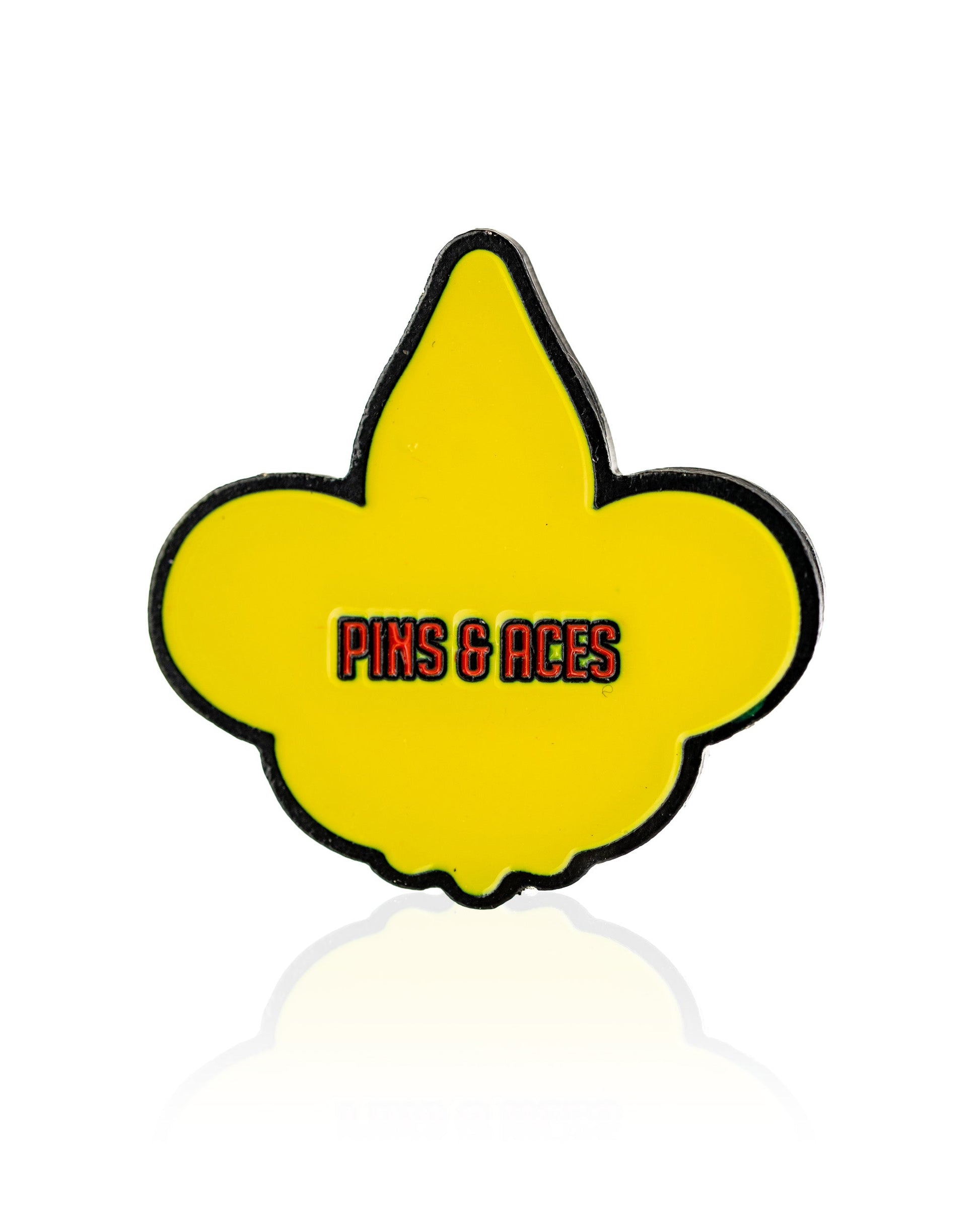 The Fleur-de-lis Ball Marker by Pins and Aces features a yellow fleur-de-lis with a black outline, plus Pins and Aces in red and black text at the center—an eye-catching premium golf accessory, shown on a white background.