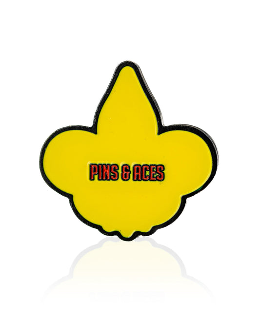 The Fleur-de-lis Ball Marker by Pins and Aces features a yellow fleur-de-lis with a black outline, plus Pins and Aces in red and black text at the center—an eye-catching premium golf accessory, shown on a white background.