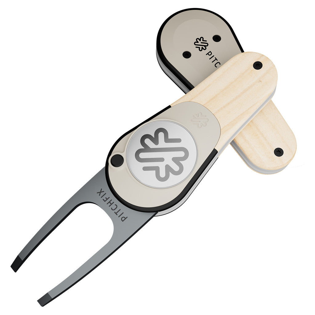 The PitchFix Woodie Divot Tool features a metal fork, light wood-effect handle, and a circular leaf logo. "PITCHFIX" is engraved on the fork, highlighting the brand’s signature style.