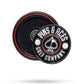 The Pop Out Medallion Ball Marker - Black by Pins and Aces is a round black and silver magnetic marker with brand text and spade symbol, stored in a matching black circular case with red trim.