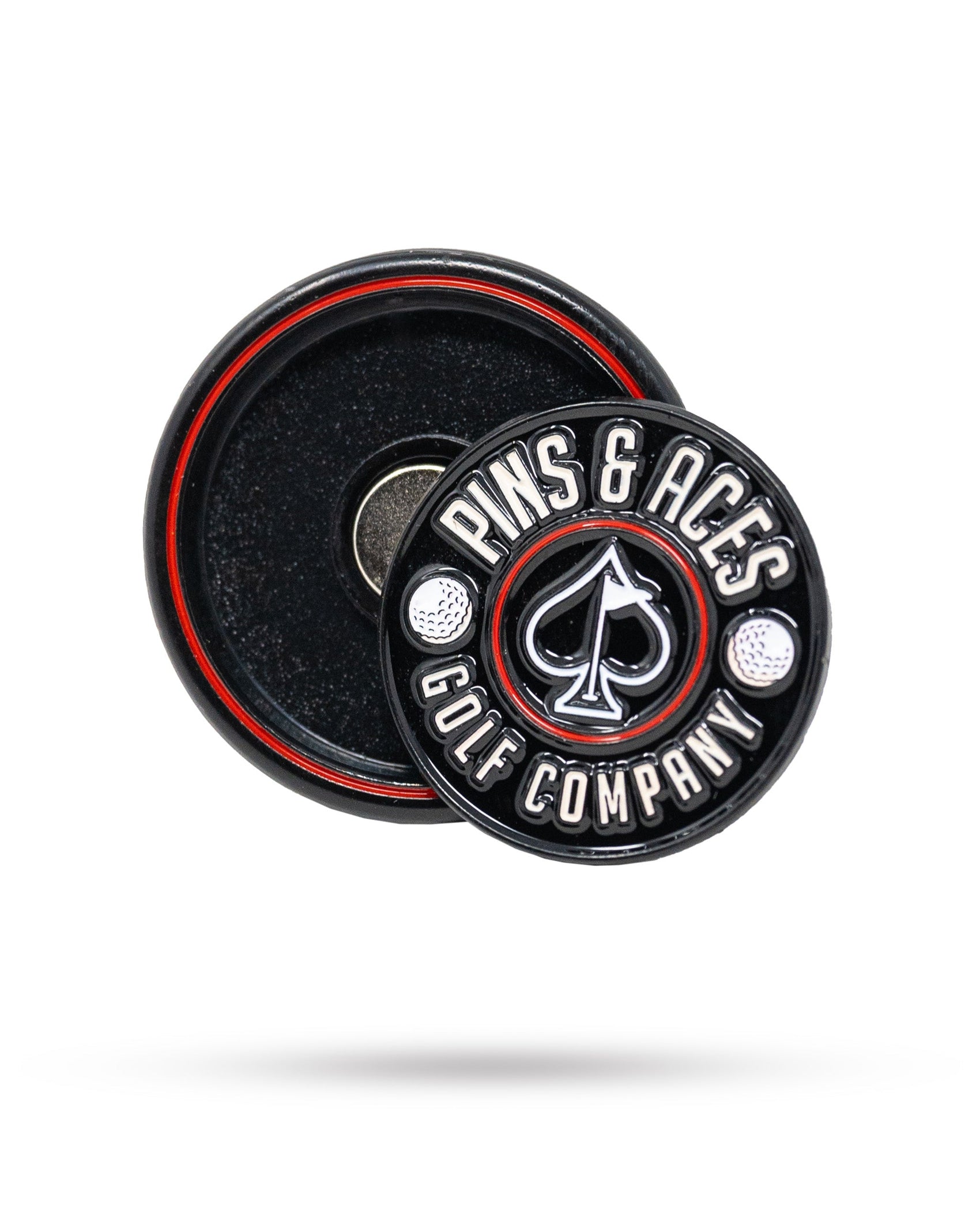 The Pop Out Medallion Ball Marker - Black by Pins and Aces is a round black and silver magnetic marker with brand text and spade symbol, stored in a matching black circular case with red trim.