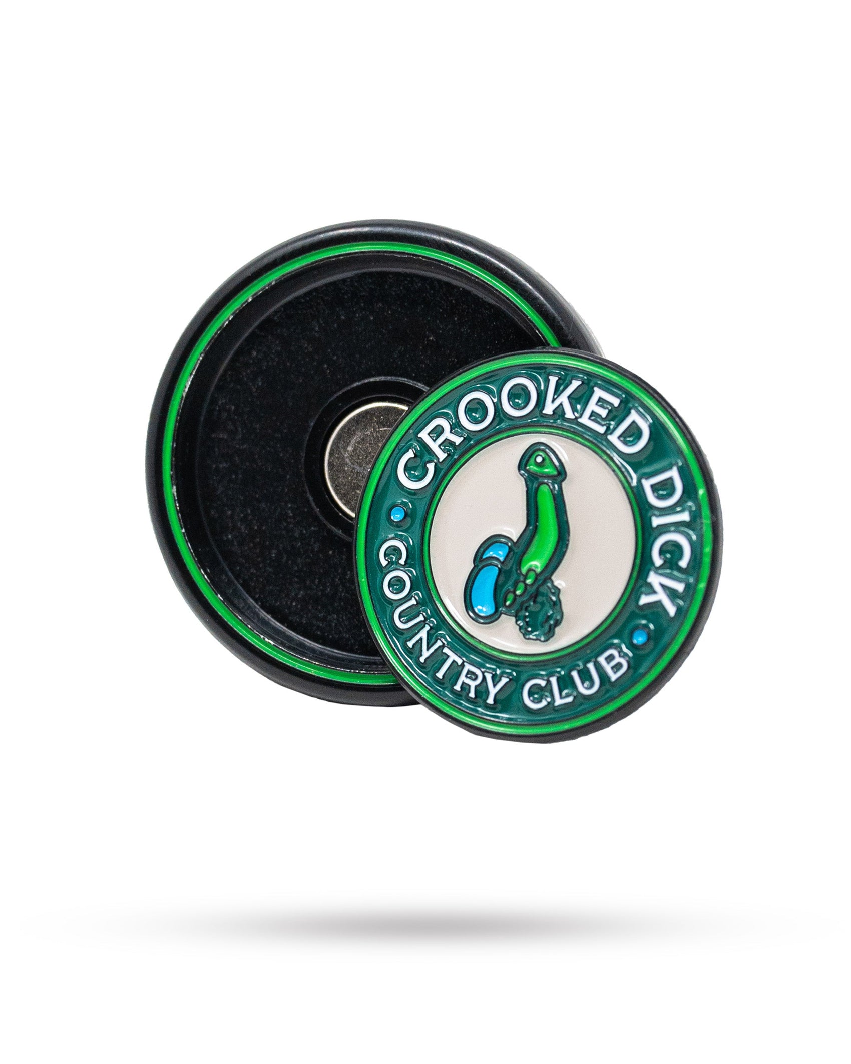 The Pop Out Medallion Ball Marker - Crooked Dick by Pins and Aces is a round green and white magnetic marker with "CROOKED DICK COUNTRY CLUB" text and a cartoon bent penis, shown next to its black case.
