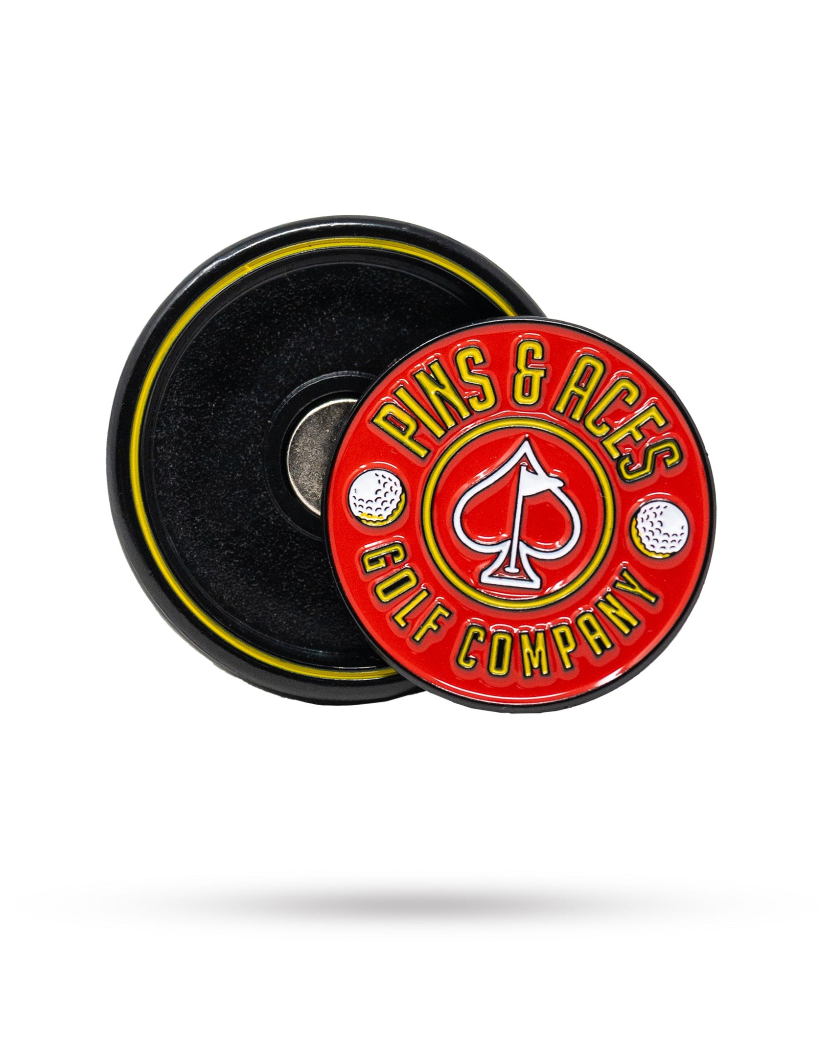 The Pins and Aces Pop Out Medallion Ball Marker - Red features a round, red and yellow design with "PINS & ACES GOLF COMPANY" text and an ace of spades symbol, positioned on a black magnetic base.