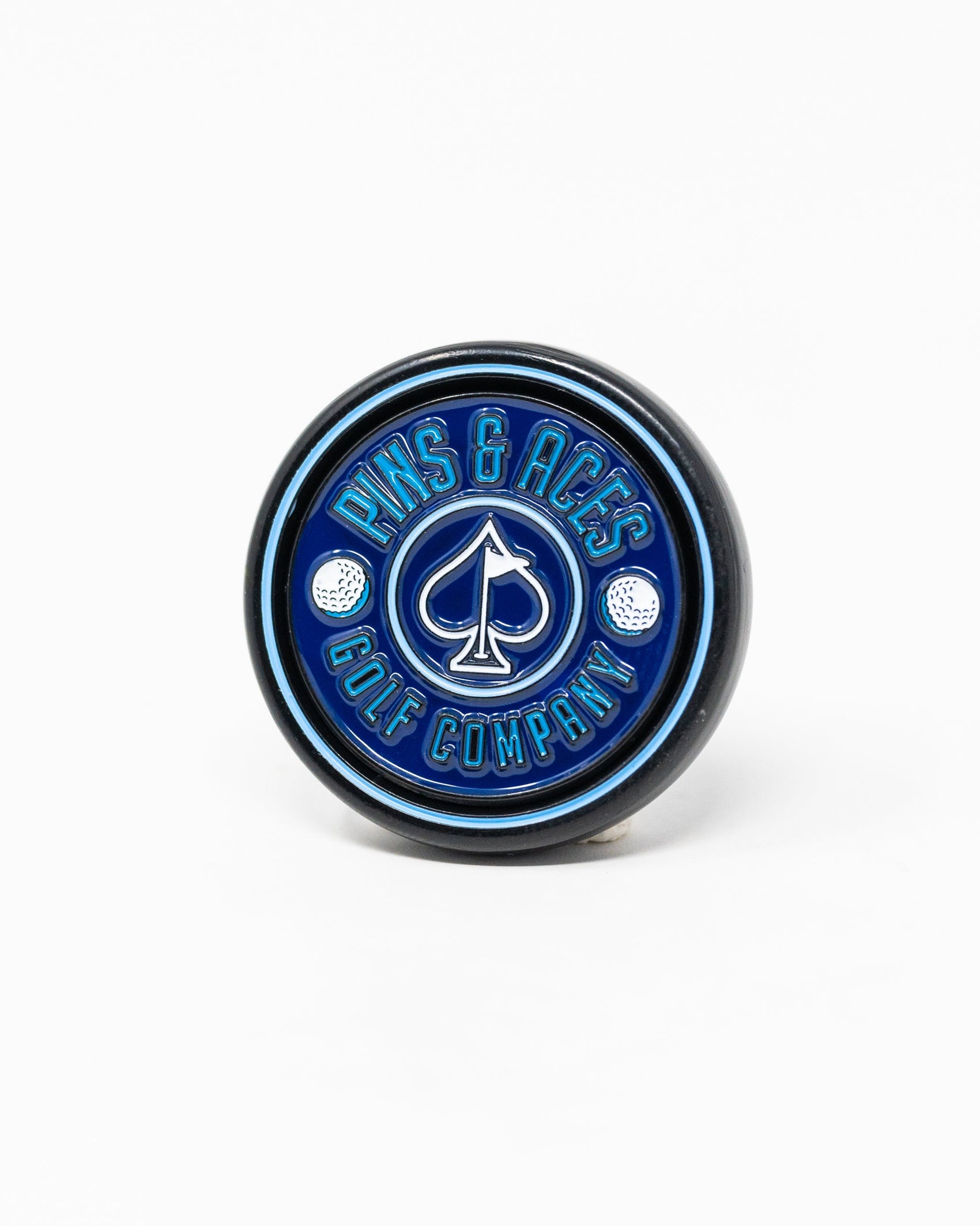 The Pop Out Medallion Ball Marker - Navy by Pins and Aces is a round blue magnetic marker featuring the brand’s name and an ace of spades in the center, flanked by two small golf balls.