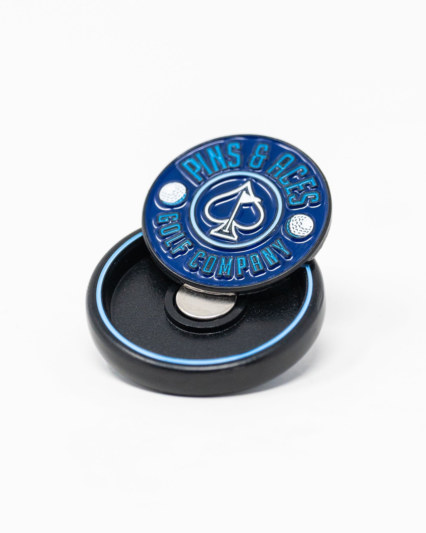 The Pop Out Medallion Ball Marker - Navy by Pins and Aces is a slim blue and silver magnetic marker, shown upright with two golf balls on a small black circular case.