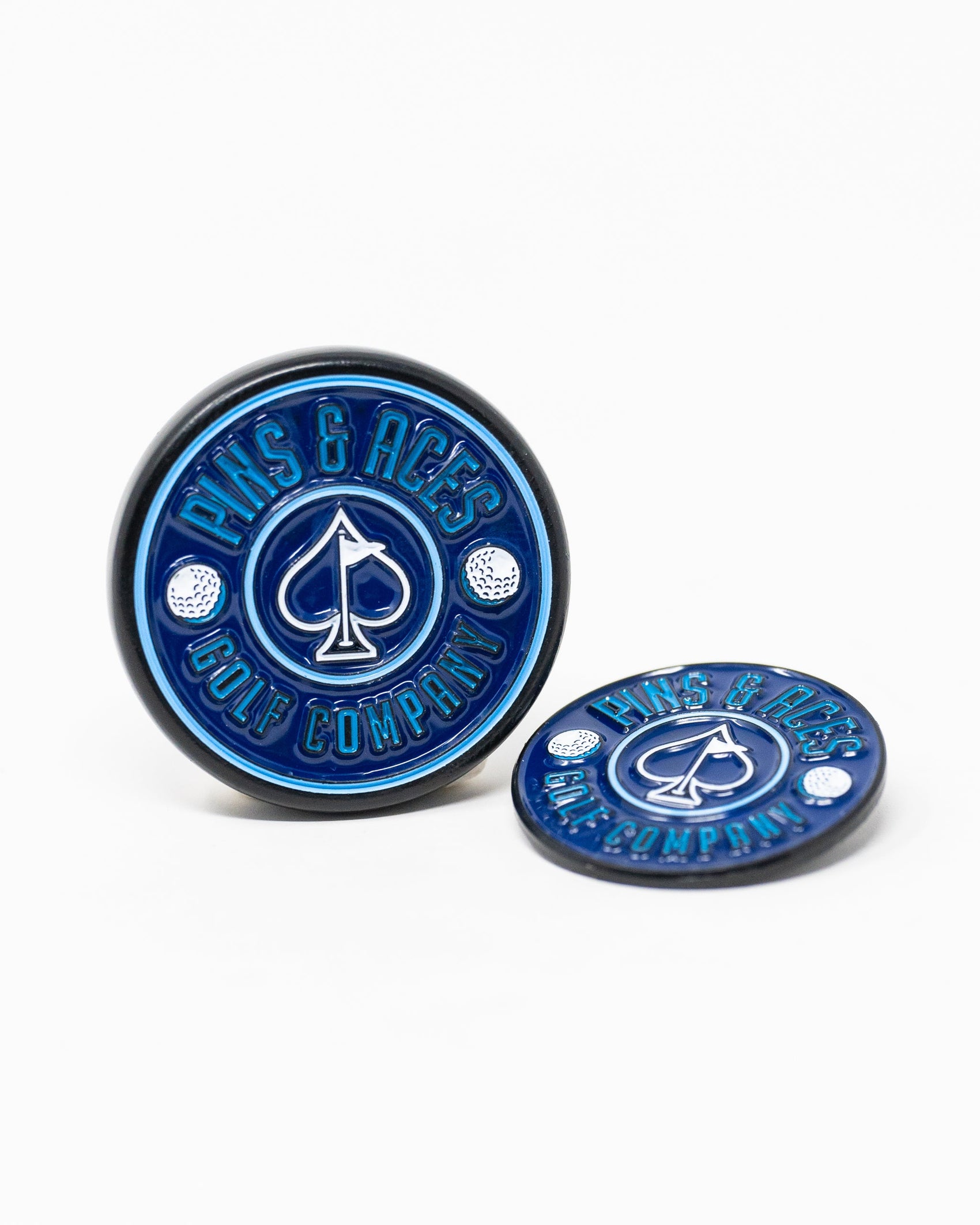 Two round, navy Pop Out Medallion Ball Markers by Pins and Aces are shown on a white background. Both feature white accents, a spade symbol, and brand text; one marker stands upright while the other lies flat.