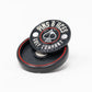 The Pop Out Medallion Ball Marker - Black by Pins and Aces, featuring an ace of spades logo, sits on its matching magnetic holder. This black and red golf accessory is displayed against a white background.