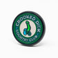 The Pop Out Medallion Ball Marker - Crooked Dick by Pins and Aces is a round green and black marker with "CROOKED DICK COUNTRY CLUB" around the edge, a cartoon snake in the center, and a convenient pop-out design.