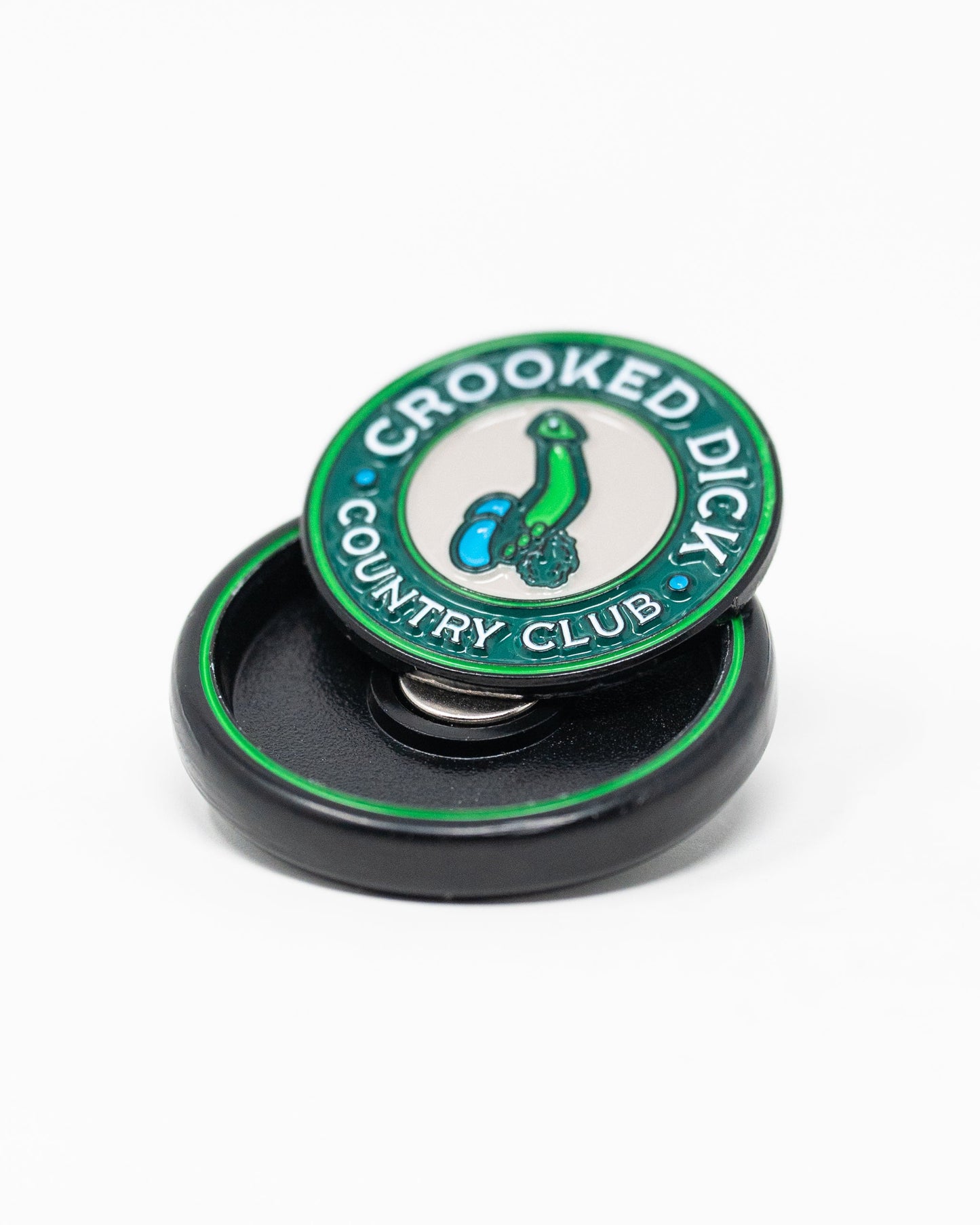 The Pop Out Medallion Ball Marker - Crooked Dick by Pins and Aces features "CROOKED DICK COUNTRY CLUB" encircling a cartoon bent green golf club with two blue balls, and comes in a sleek black round case.