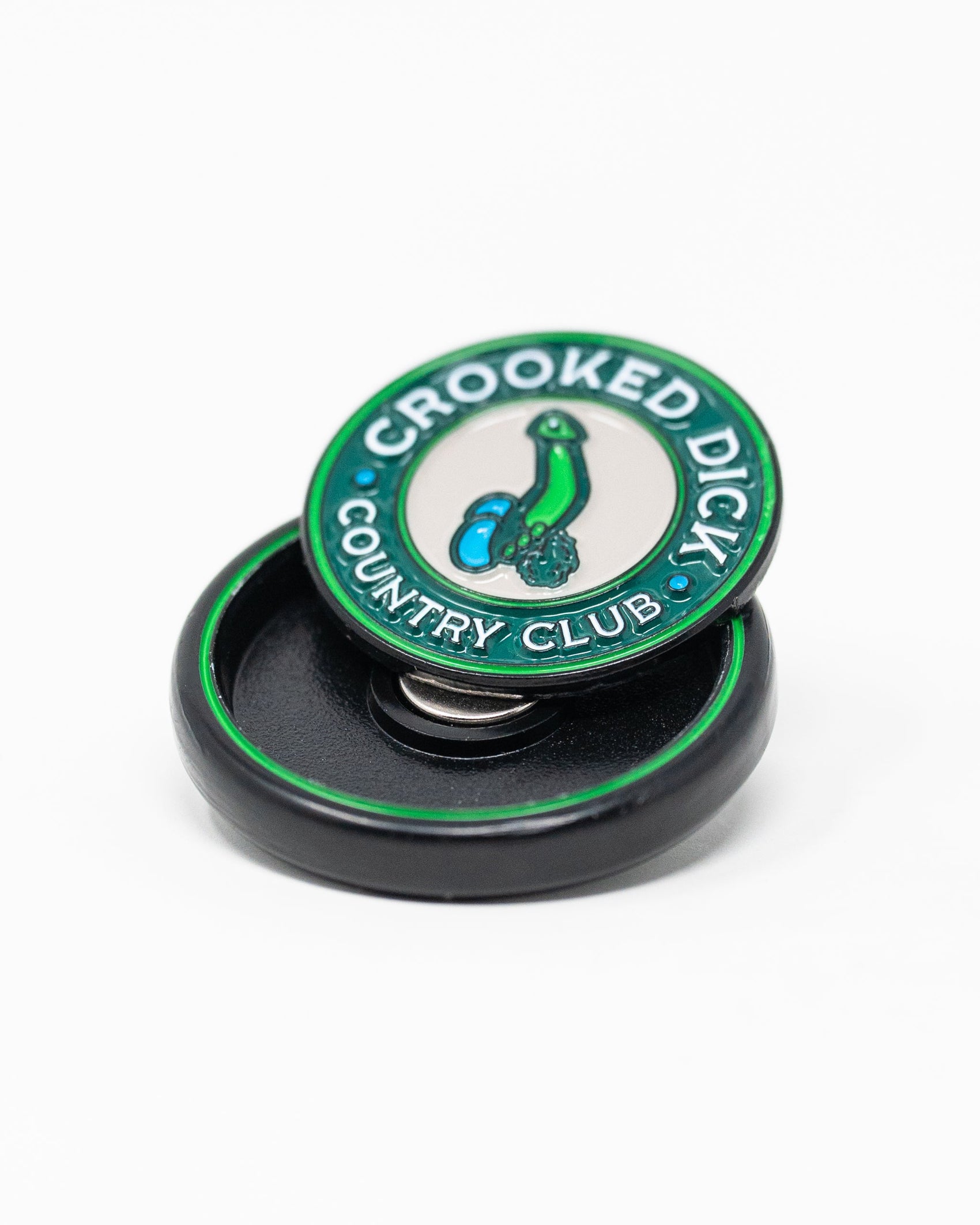 The Pop Out Medallion Ball Marker - Crooked Dick by Pins and Aces features "CROOKED DICK COUNTRY CLUB" encircling a cartoon bent green golf club with two blue balls, and comes in a sleek black round case.